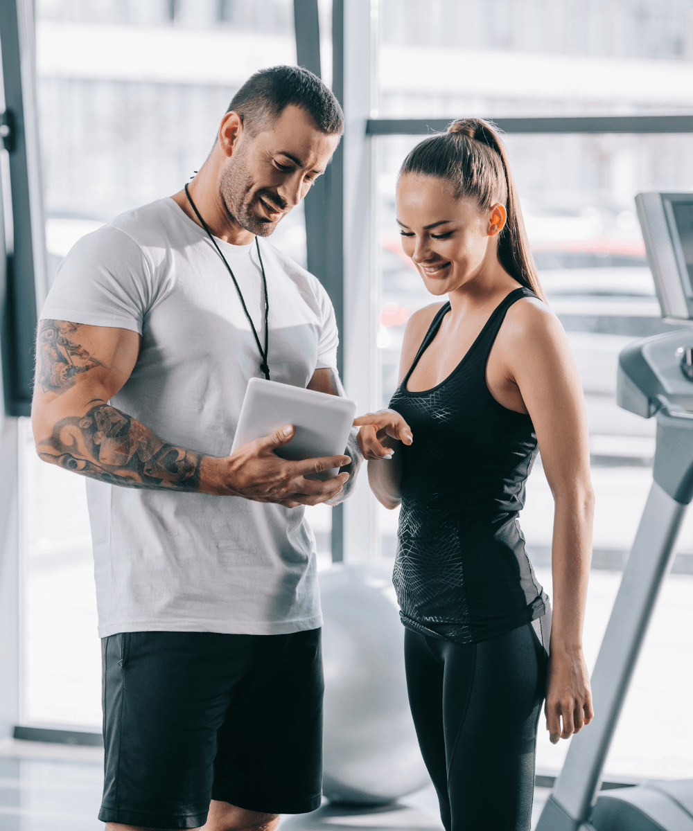 A male gym owner stands with female gym member while looking at tablet used to showcase member retention